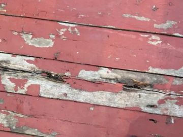 Worn, peeling red and white paint on wooden planks.