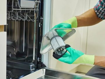 Person cleaning a dishwasher filter wearing protective gloves.