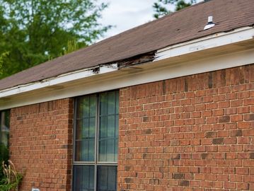 Damaged eaves on a brick house with visible wood rot and missing sections.