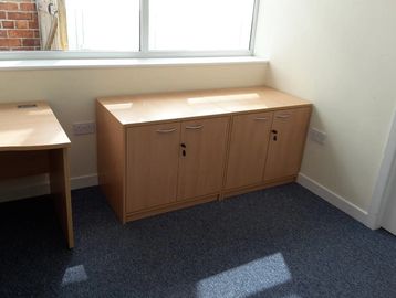 Two wooden cabinets with locks under a window in an office room.