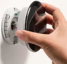 Hand adjusting a round thermostat on a wall.