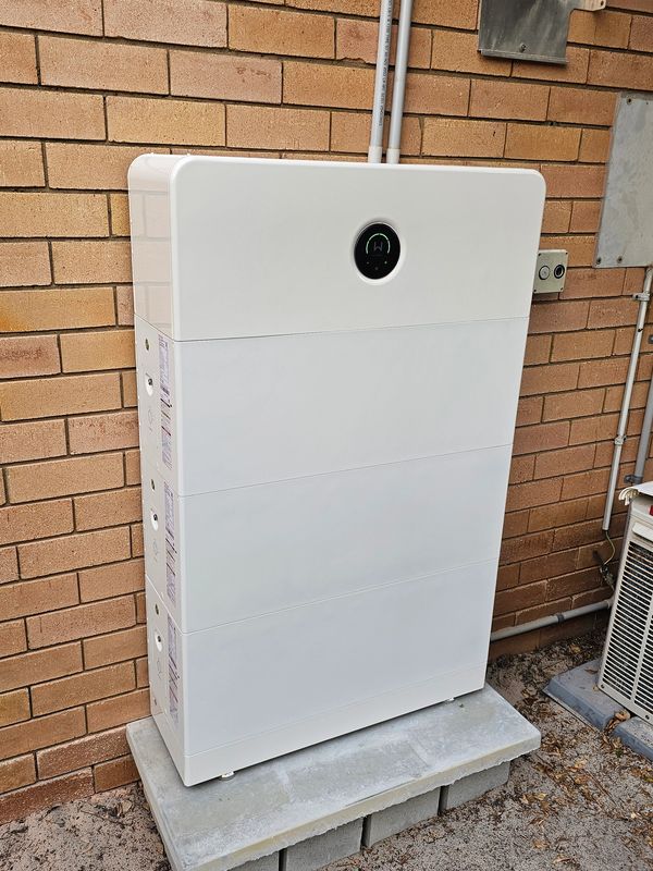 White battery storage unit installed against a brick wall.