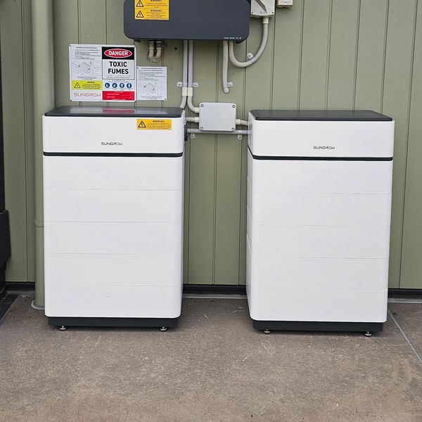 Two white SunGrow energy storage units installed outdoors against a green wall.