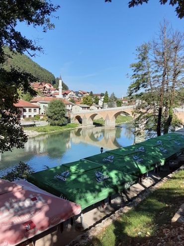 Historic stone bridge over calm river in a quaint village under clear blue sky.