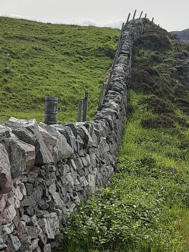Curved stone wall on a grassy hillside with wooden fence posts.