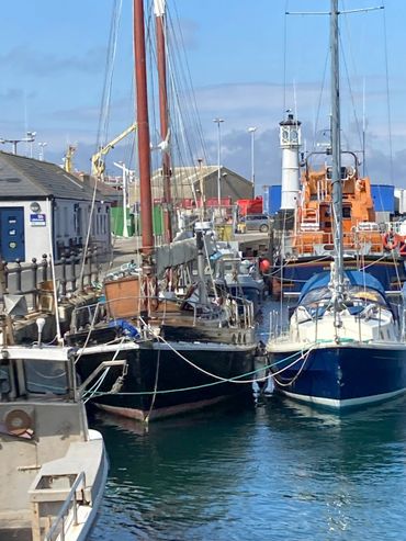 Boats docked in a busy harbor with a lighthouse in the background.