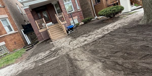 A freshly prepared soil yard in front of a brick house with stairs and bushes.