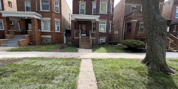 Row of brick houses with front porches and a tree in the yard.