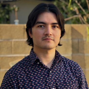 Young man with medium-length hair in patterned shirt outdoors.