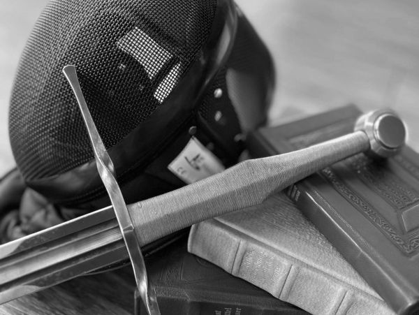 Fencing mask, sword, and old books stacked together.