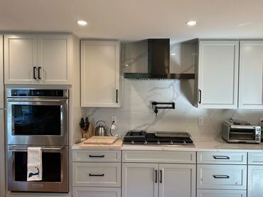 Modern kitchen with white cabinets, stainless steel oven, and marble backsplash.