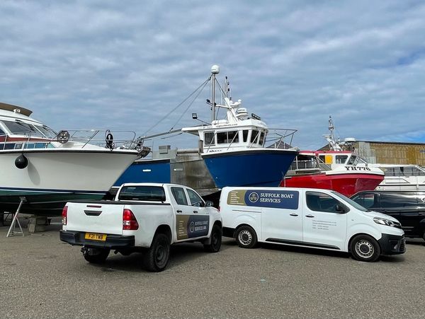 Boats on dry dock with service vehicles parked nearby under cloudy sky.