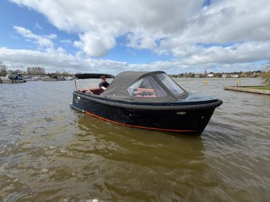 A black motorboat with a canopy on a calm lake under a cloudy sky.
