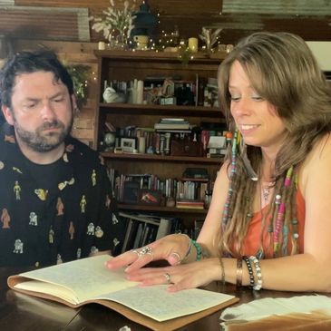 Two people reading a book together at a wooden table in a cozy room.