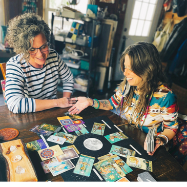 Two women engaged in a joyful tarot card reading session indoors.