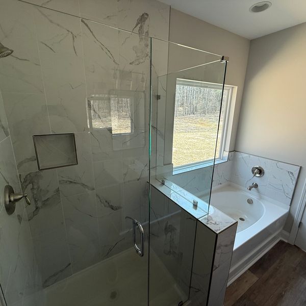 Modern bathroom with glass shower and bathtub by a window.