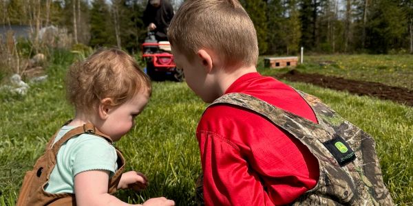 Two young children playing in the grass outdoors.