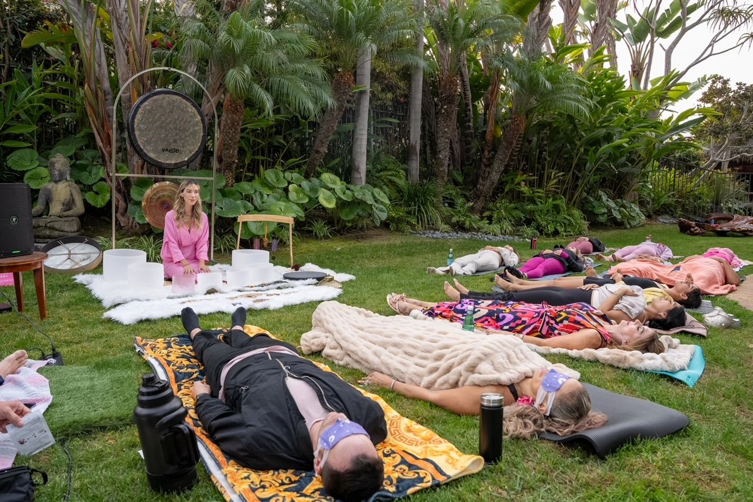 People lying on mats in a garden during a sound healing session.