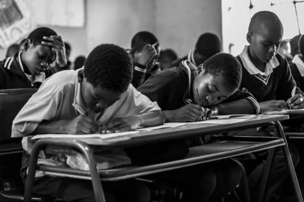 Students intensely focused on writing during an exam in a classroom.