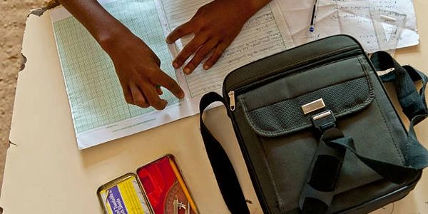 Hands pointing at a notebook on a desk with stationery and a bag.