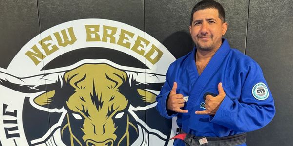 Man in blue martial arts gi posing with hand signs in front of a bull logo.