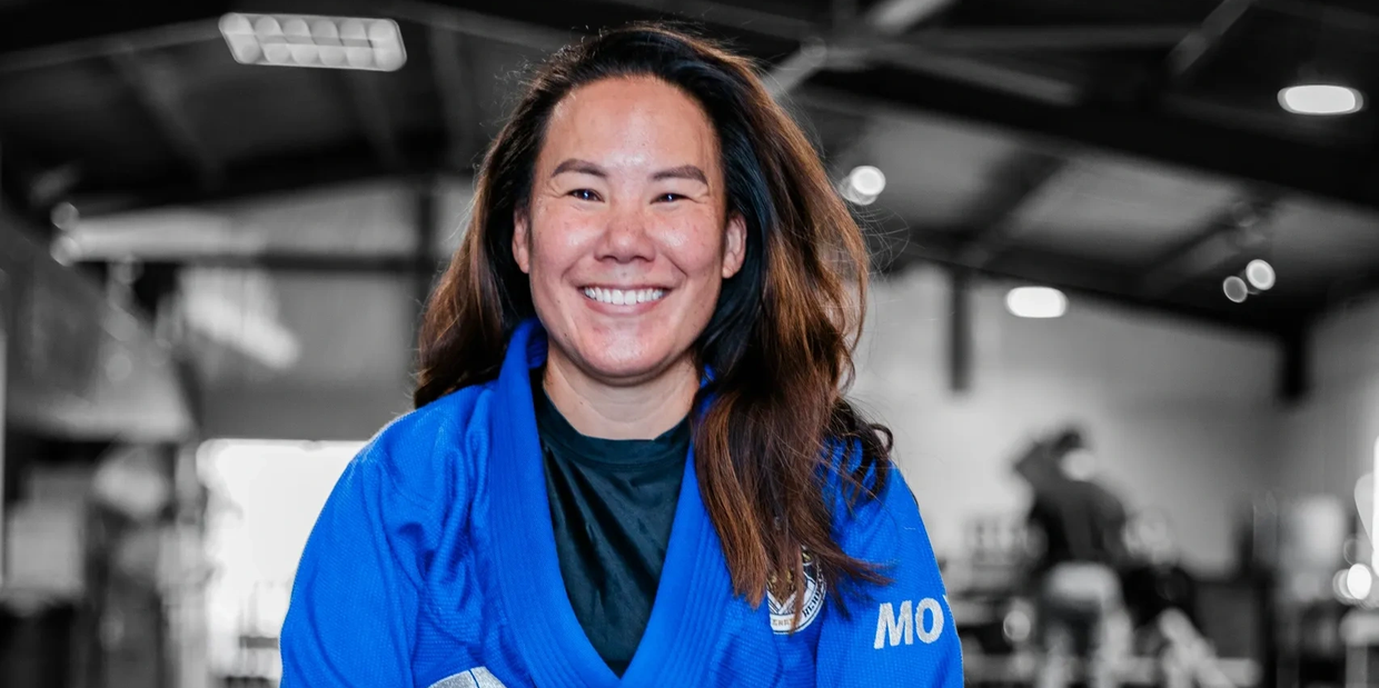 Smiling woman in a blue martial arts gi in a gym setting.