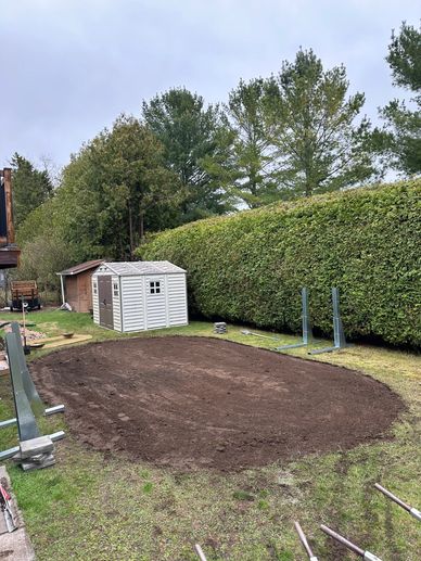 A freshly dug backyard area with sheds and metal stands nearby.