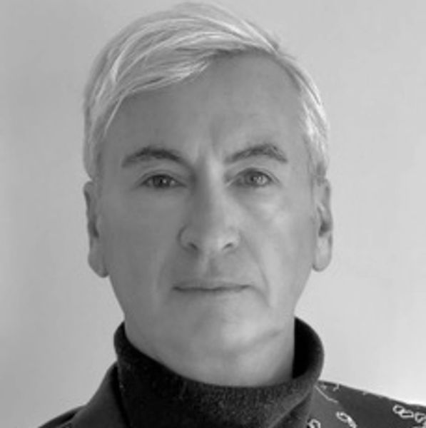 Portrait of a man with blonde hair in a black turtleneck and patterned jacket.