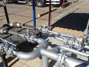 Industrial metal pipes and valves arranged outdoors on tiled flooring.