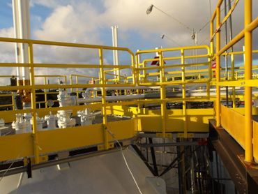 Industrial facility with yellow safety railings and pipes under a partly cloudy sky.