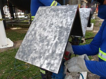 Workers handling a metal piece with protective gloves outdoors.