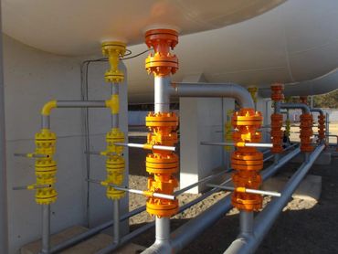 Industrial pipes with yellow and orange valves connected to a large tank.
