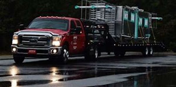 Red truck towing large glass panels on a trailer during rainy weather.