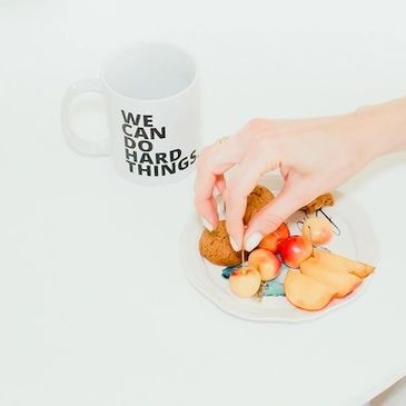 Hand picking fruit from a plate next to a motivational mug.