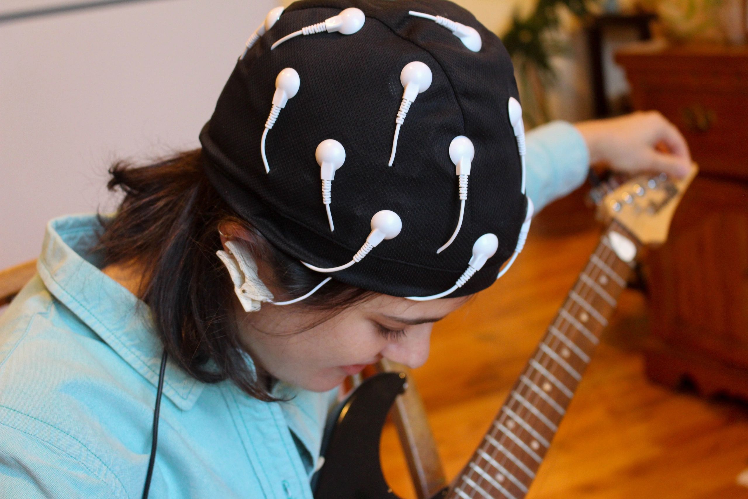 Person wearing EEG cap while playing guitar.