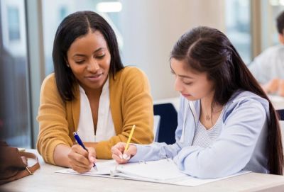 Teacher helping student with schoolwork at a desk.