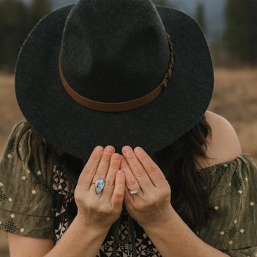 Person hiding face behind a wide-brimmed hat in a scenic outdoor setting.