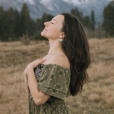 Woman in green dress enjoying nature with eyes closed and hands near heart.