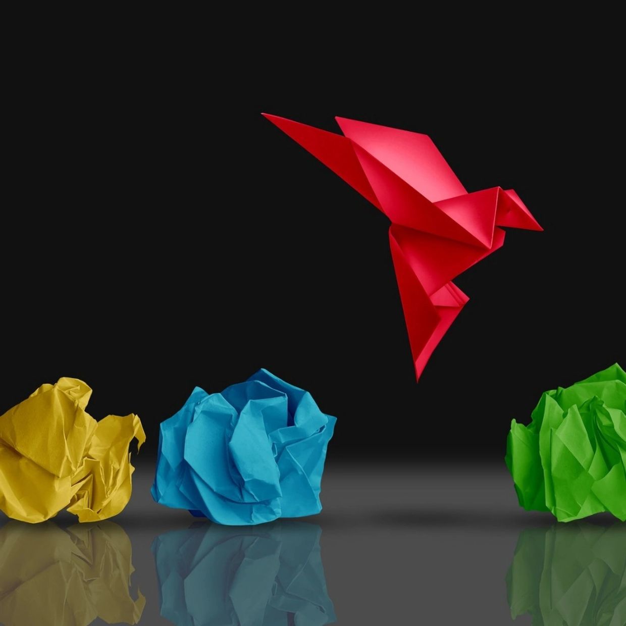 Red paper bird flying away from other coloured scrunched paper.