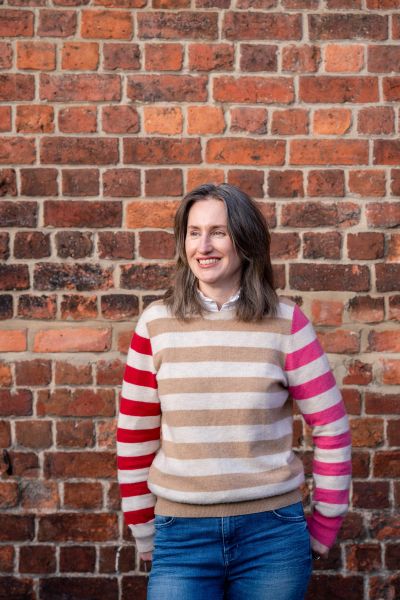Woman in a striped sweater stands against a brick wall smiling.