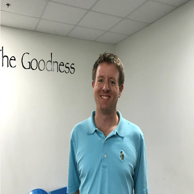 Man in a light blue polo shirt smiling in a fitness room.