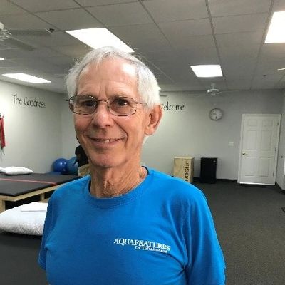 Smiling elderly man in blue Aquatic Fitness shirt indoors.