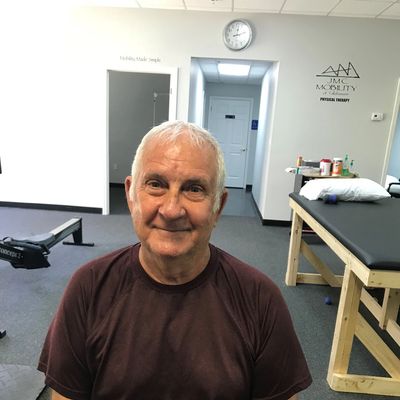 Smiling elderly man sitting in a physical therapy clinic.