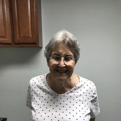 Smiling elderly woman in glasses and a white shirt with red polka dots.