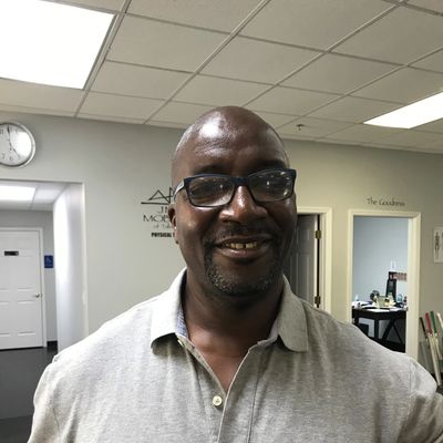 Smiling man wearing glasses and a gray polo shirt indoors.