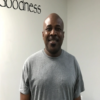 Smiling man in gray t-shirt standing indoors near a blue exercise ball.