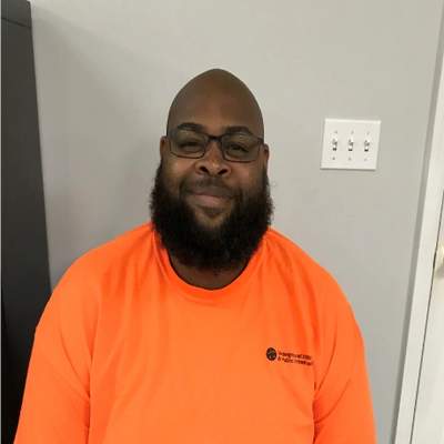 A man with glasses and a beard wearing a bright orange shirt sitting indoors.