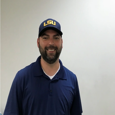 Smiling man wearing a navy blue LSU cap and polo shirt against a plain background.