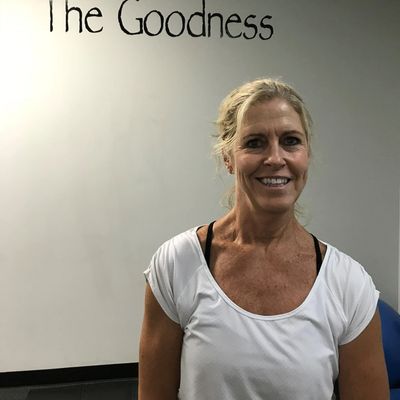 Smiling woman in a white shirt with "The Goodness" written on the wall behind her.