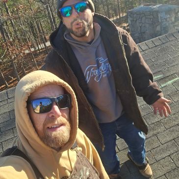 Two men wearing sunglasses on a rooftop with trees in the background.